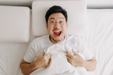 Happy smiling asian man lie down on white bed.