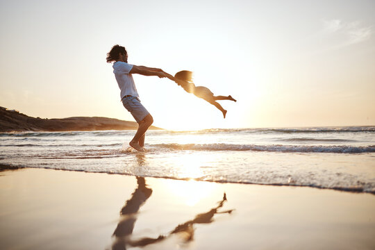 Father, spin girl kid and beach with games, holding hands or sunset for bonding together by waves. Dad, female kid and swing for love, care or play by sea, silhouette or family on vacation in summer