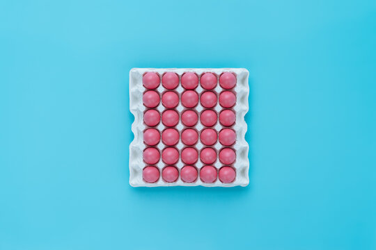 Still life of thirty bright pink Easter eggs in white egg carton against turquoise background, directly above view 