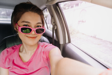 Happy asian women wear pink shirt take selfie wear sunglasses smiling in the car