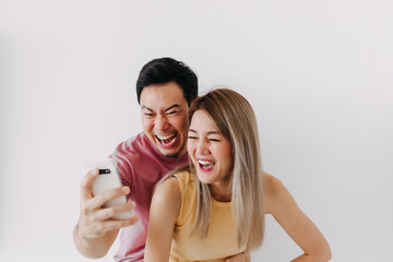 Happy asian couple lover laughing at the news content in the smartphone isolated on white.