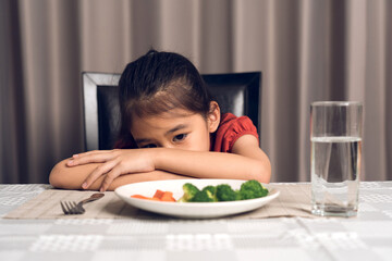 Little cute kid girl refusing to eat healthy vegetables. Children do not like to eat vegetables. - obrazy, fototapety, plakaty