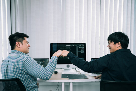 Asian employee software developers celebrate success project by fist bump in office room.