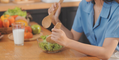 A young woman with a beautiful face in a blue shirt with long hair eating fruit sitting inside the kitchen at home with a laptop and notebook for relaxation, Concept Vacation.