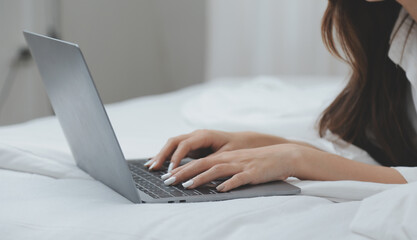 Naklejka premium Happy young female in casual clothes smiling and looking at camera while using laptop on bed in bedroom at home