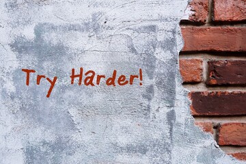 A grunge vintage brick wall and grey cement with hand written text TRY HARDER, concept of never...