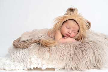 Baby Junge Newborn mit Löwen Mütze liegend auf grauem Fell in einem Eimer, weißer Hintergrund...