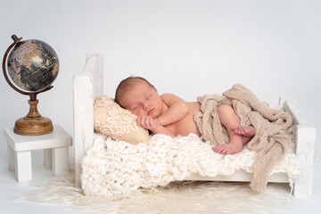 Baby Junge Newborn liegend im Bett mit Dekoration Weltkugel in einem Eimer, weißer Hintergrund...