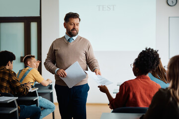 Mature teacher handing over test results to his students in classroom.