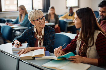 Happy mature woman talking to younger classmate during educational course in classroom.