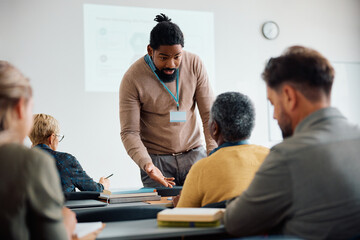 Black teacher talks to senior man during adult education training class in lecture hall.