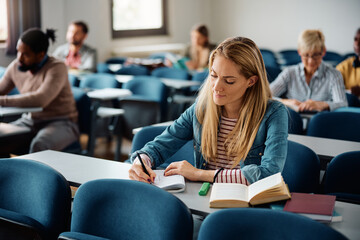 Mid adult woman writes in notebook while attending class at university