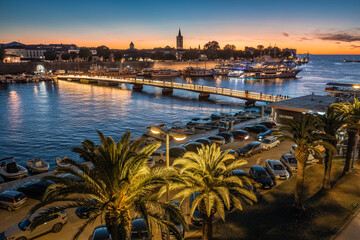 Zadar, Croatia - Aerial view of palm trees at the city of Zadar at golden sunset sky with illuminated City Bridge (Gradski most), Cathedral of St. Anastasia tower and yacht marina