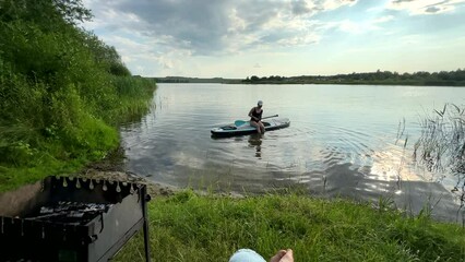 cooking meat on fire near lake woman supboarding on background