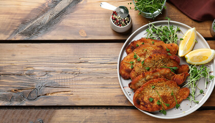 Tasty schnitzels served with lemon and microgreens on wooden table, flat lay. Space for text