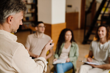 Adult male teacher talking with group of students during lecture in library