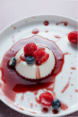 Panna cotta with cherry sauce splashes, raspberry and blueberry. Italian dessert with cream, milk, vanilla and gelatine on a white plate. Restaurant modern serving, food styling. Top view