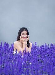 Asian woman in white dress sitting amidst in flowers field. Beautiful girl holding bouquet flowers in hands. Happy woman enjoying in purple flower field and nature sea of fog. Embrace nature,wind.