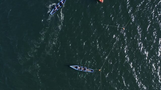 Drone rises to bird's eye view perspective with currach irish canoe boats tethered to buoys in open ocean