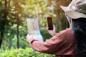 Hiking elderly woman in autumn nature holding map and smartphone outdoors  in the sunlight.