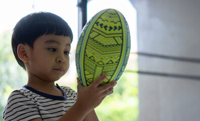 Portrait of Asian boy holding american football and looking with interested.