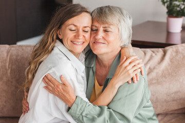Older mature mother and grown millennial daughter laughing embracing, caring smiling young woman embracing happy senior middle aged mom