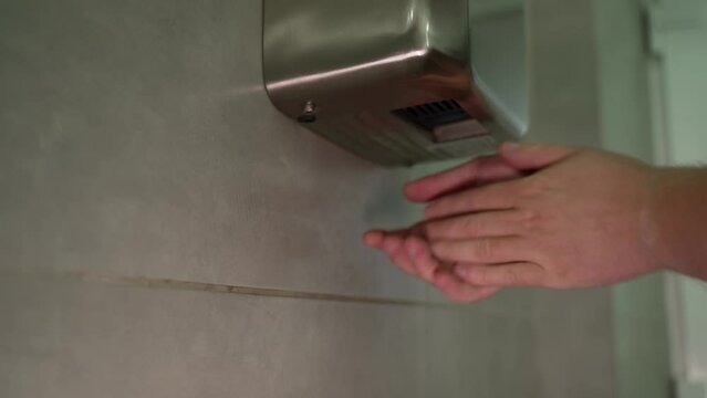 new stylish washroom with ceramic tiles on the walls and a modern hand dryer close-up of a man after washing his hands drying them under the pressure of hot air
a modern way of saving paper towels
