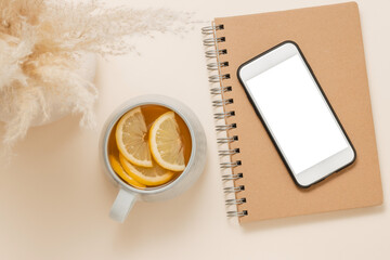Mobile phone mockup with white screen on notepad with cup of tea with lemon. Feminine home office desk, aesthetic mobile background. Smartphone template for design and branding, website promotion