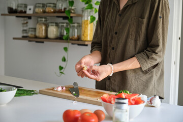 Unrecognizable asian young man peeling garlic at kitchen.