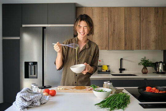 Smiling asian young man beating eggs at kitchen.