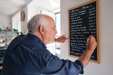 Smiling cafe owner writing menu on black board with pen