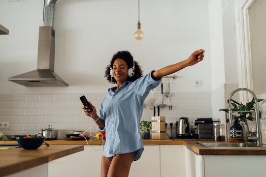 Woman dancing and listening music in the morning in her kitchen