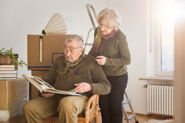 Senior couple looking at photo album surrounded by cardboard boxes in an empty room