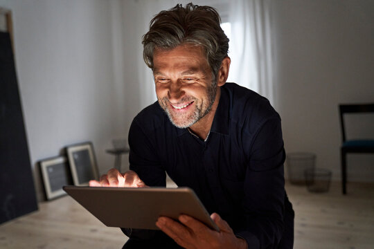 Portrait of smiling mature man having fun with digital tablet at home