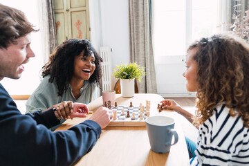 Parents sitting in livingroom teaching daughter to play chess
