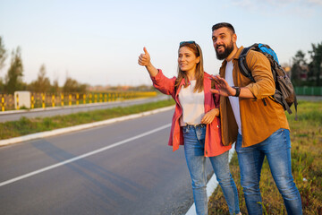 Happy couple hitchhiking on roadside trying to stop car.