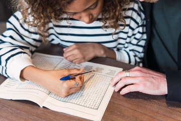 Father observing daughter solving a puzzle in a puzzle book