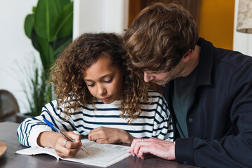 Father observing daughter solving a puzzle in a puzzle book