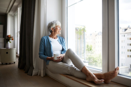 Smiling senior woman looking through window while sitting at home