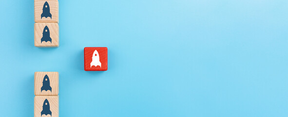 Group of wooden cubes with rocket icon in one direction and one red wooden cube with rocket icon...