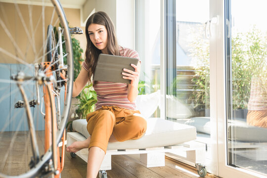 Young woman with tablet reparing bicycle at home