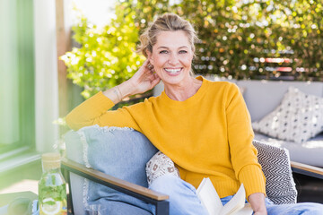 Portrait of happy mature woman sitting on terrace with book