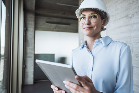 Smiling engineer wearing hardhat standing with tablet PC