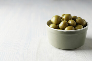 Olives in bowl on white wooden background, space for text