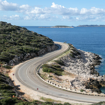 Long curved asphalt road running along the rocky shore of the Mediterranean Sea in a Turkish resort. The hilly coast is covered with forest, white stones. Endless deep blue sea on the horizon.