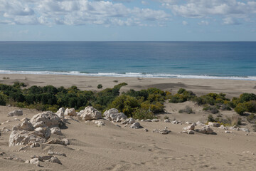 Panoramic photo of wide sandy Patara beach on the mediterranean coast in Turkey. Huge white dusty dunes, endless sea and mountain ridge in the distance.