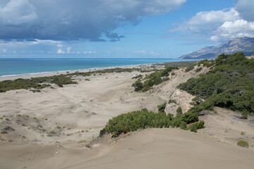 Panoramic photo of wide sandy Patara beach on the mediterranean coast in Turkey. Huge white dusty dunes, endless sea and mountain ridge in the distance.