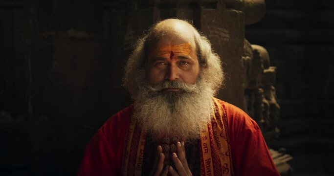 Zoom in Portrait of a Senior Hindu Monk Looking at the Camera and Smiling in an Ancient Temple. Friendly Indian Senior Man Posing as he is seeking Guidance and Wisdom from his Religion