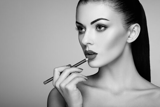 Black and white photo of woman painting lipstick. Beautiful woman face. Makeup detail. Beauty girl with perfect skin. Red lips and nails manicure