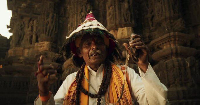 In an Ancient Hindu Temple, a Close-Up Portrait Features an Old Indian Man Adorned in Traditional Attire, Playing Instruments, and Chanting. The Senior Male Preserves the Rich Cultural Heritage